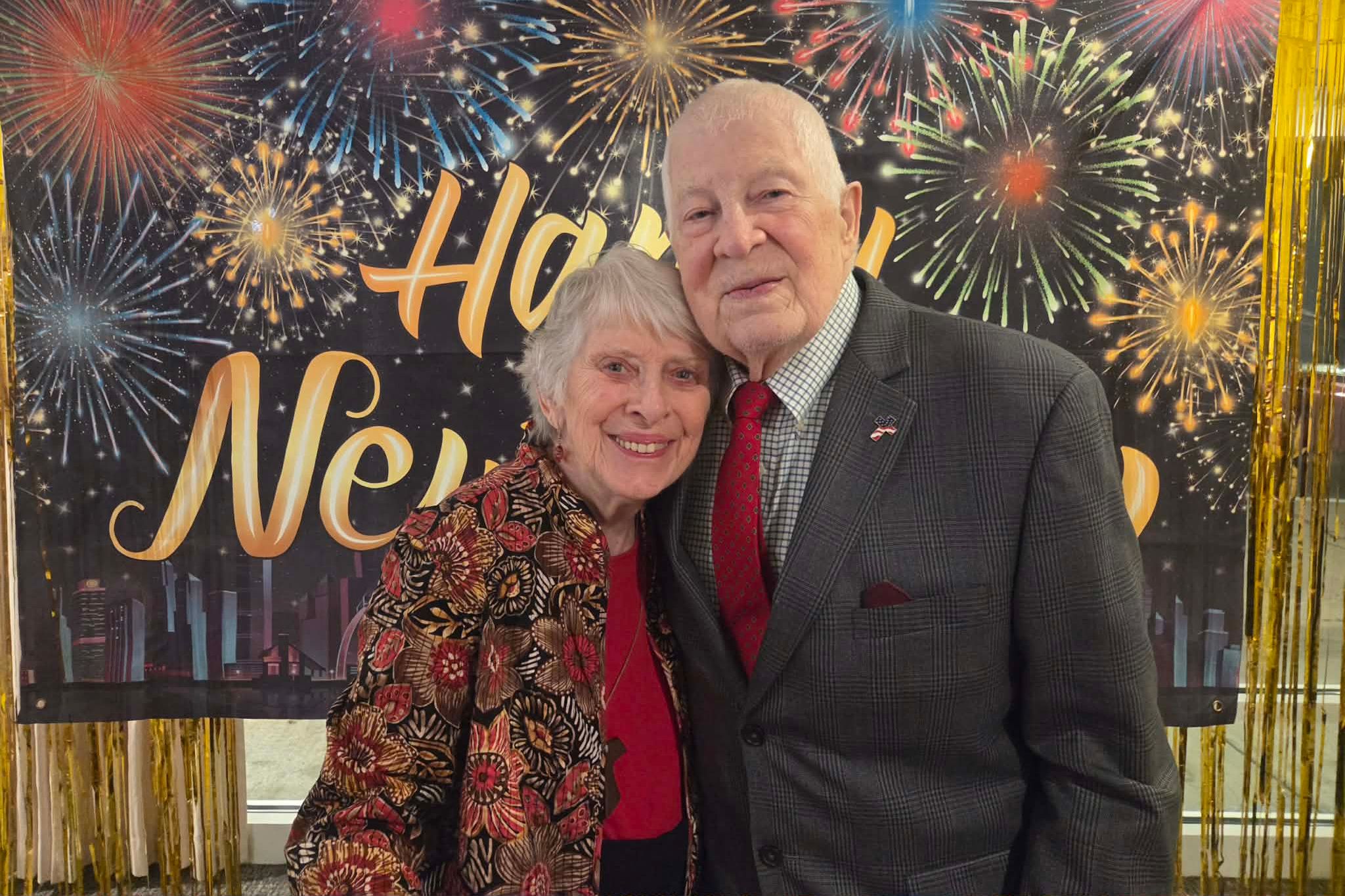 Elderly couple smiling and hugging in front of a Happy New Year fireworks backdrop, capturing a joyful moment perfect for a photo essay.
