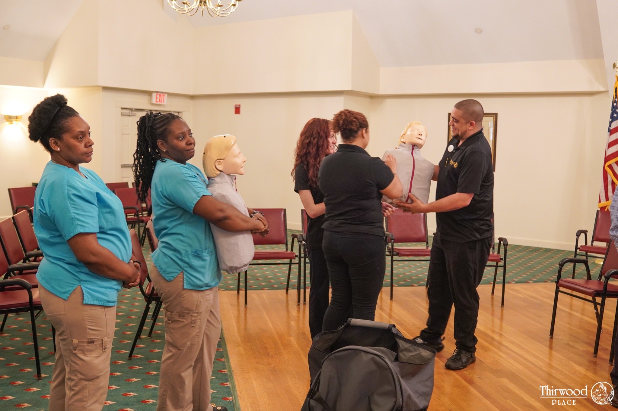Five adults stand in a room, each holding CPR mannequins during a training session focused on emergency response to food-related or cold and flu incidents.
