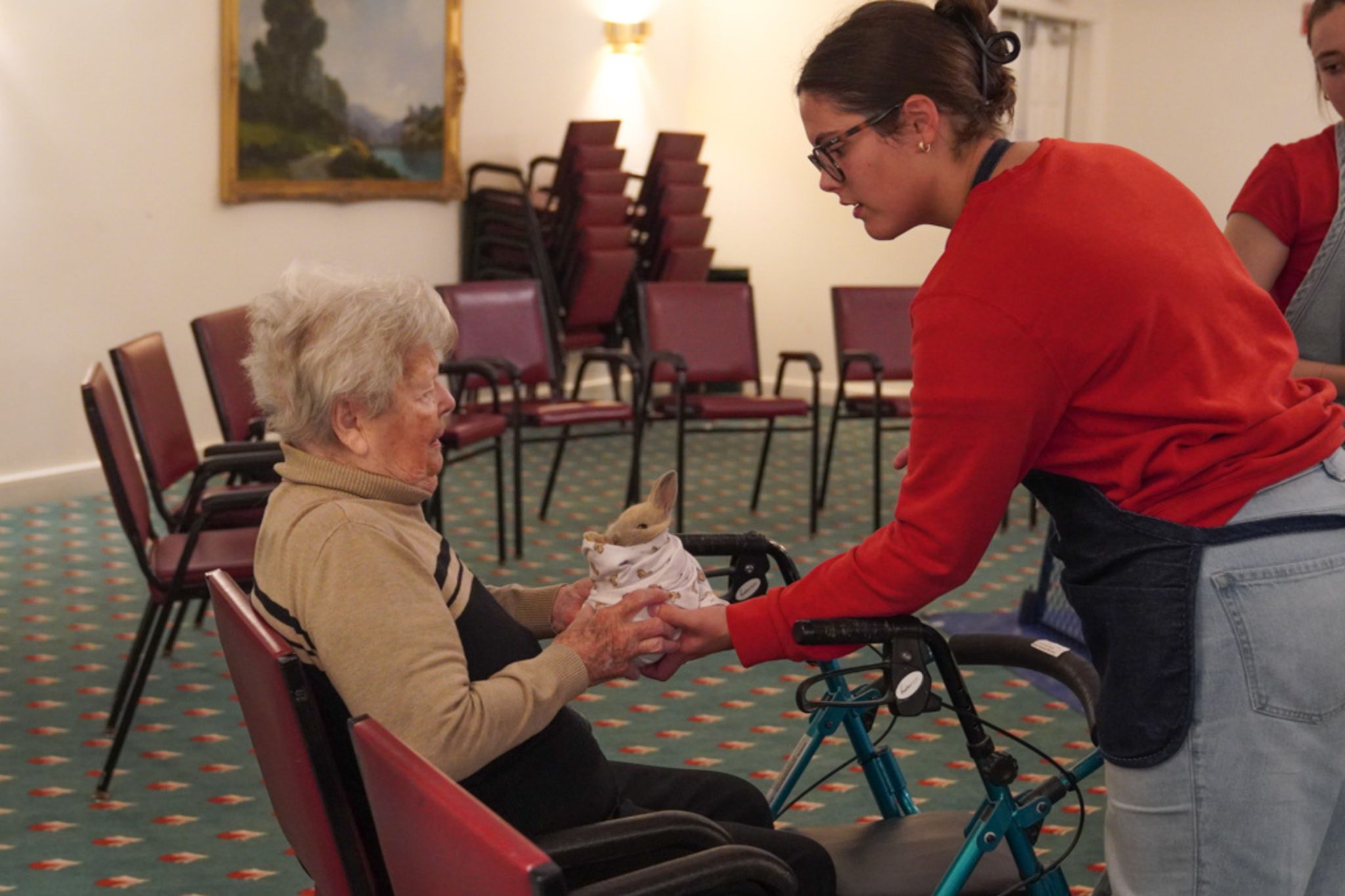 A young woman, grateful for her scholarship, helps an elderly woman in a wheelchair hold a small animal wrapped in a towel.