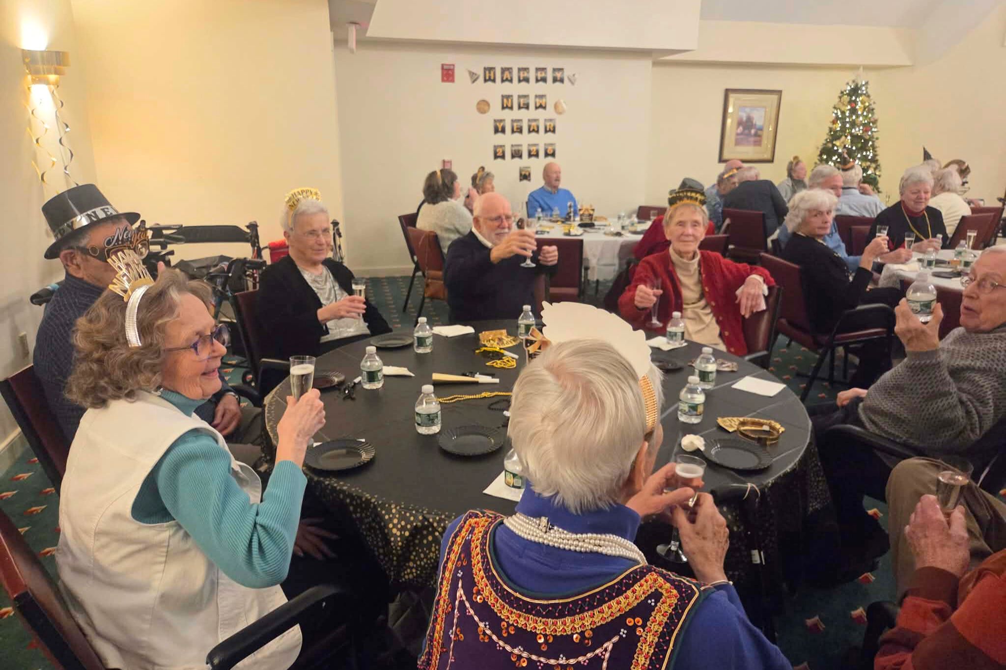 Seniors wearing party hats raise glasses at a decorated table during a festive summer holiday gathering, perfect for a cheerful photo essay.