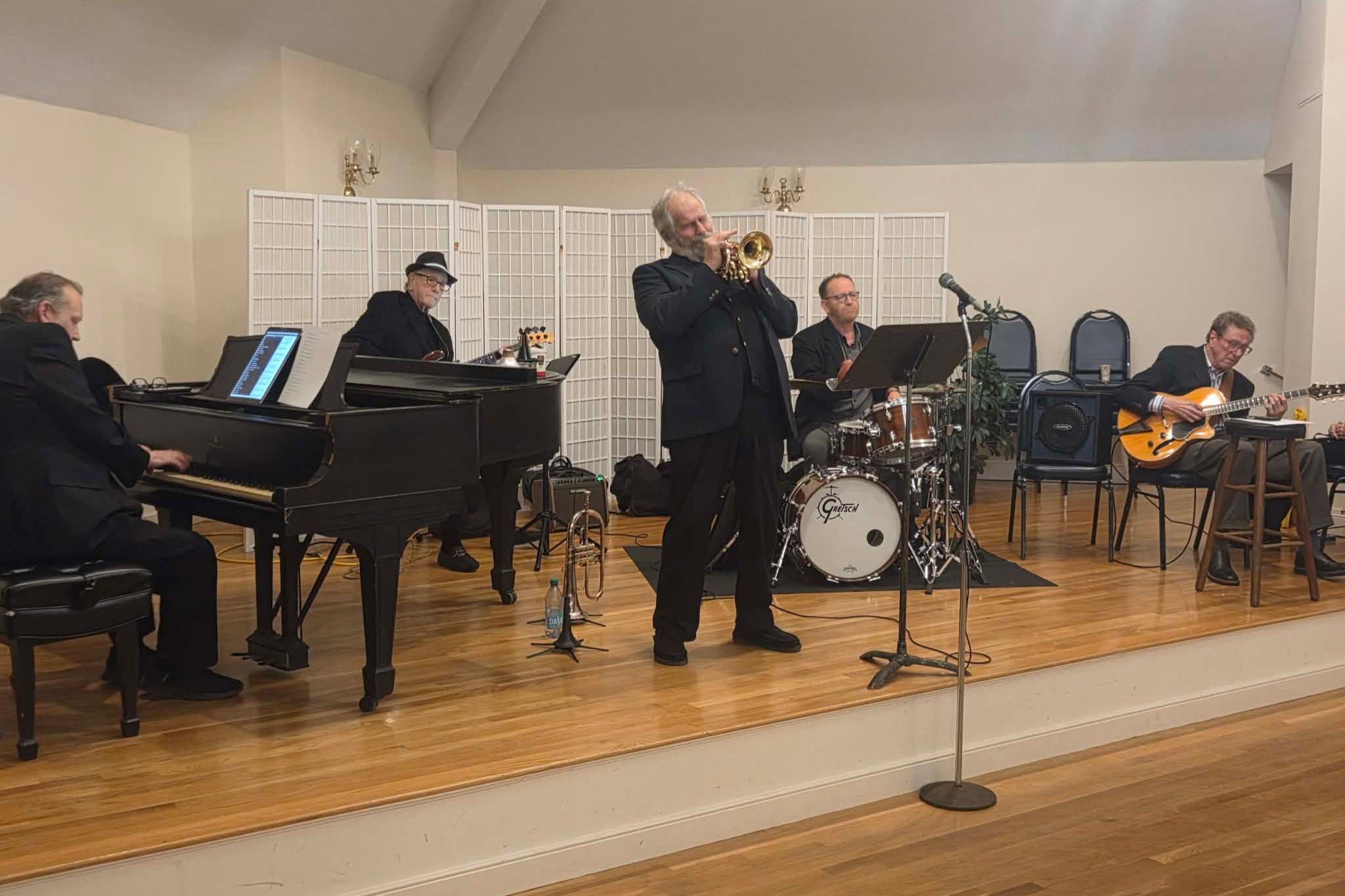 Five musicians play piano, bass, trumpet, drums, and guitar on a small indoor stage in this vibrant summer photo essay.