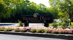 A sign reading Thirwood Place, 237 North Main Street stands amid colorful flowers, greenery, and whimsical animal sculptures.