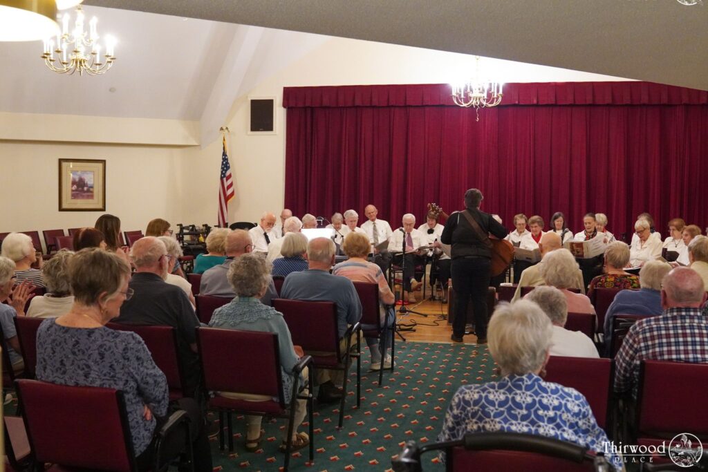 Audience watching a senior choir perform on stage in a room with red curtains and chandeliers, celebrating the winners of this year’s scholarship awards.