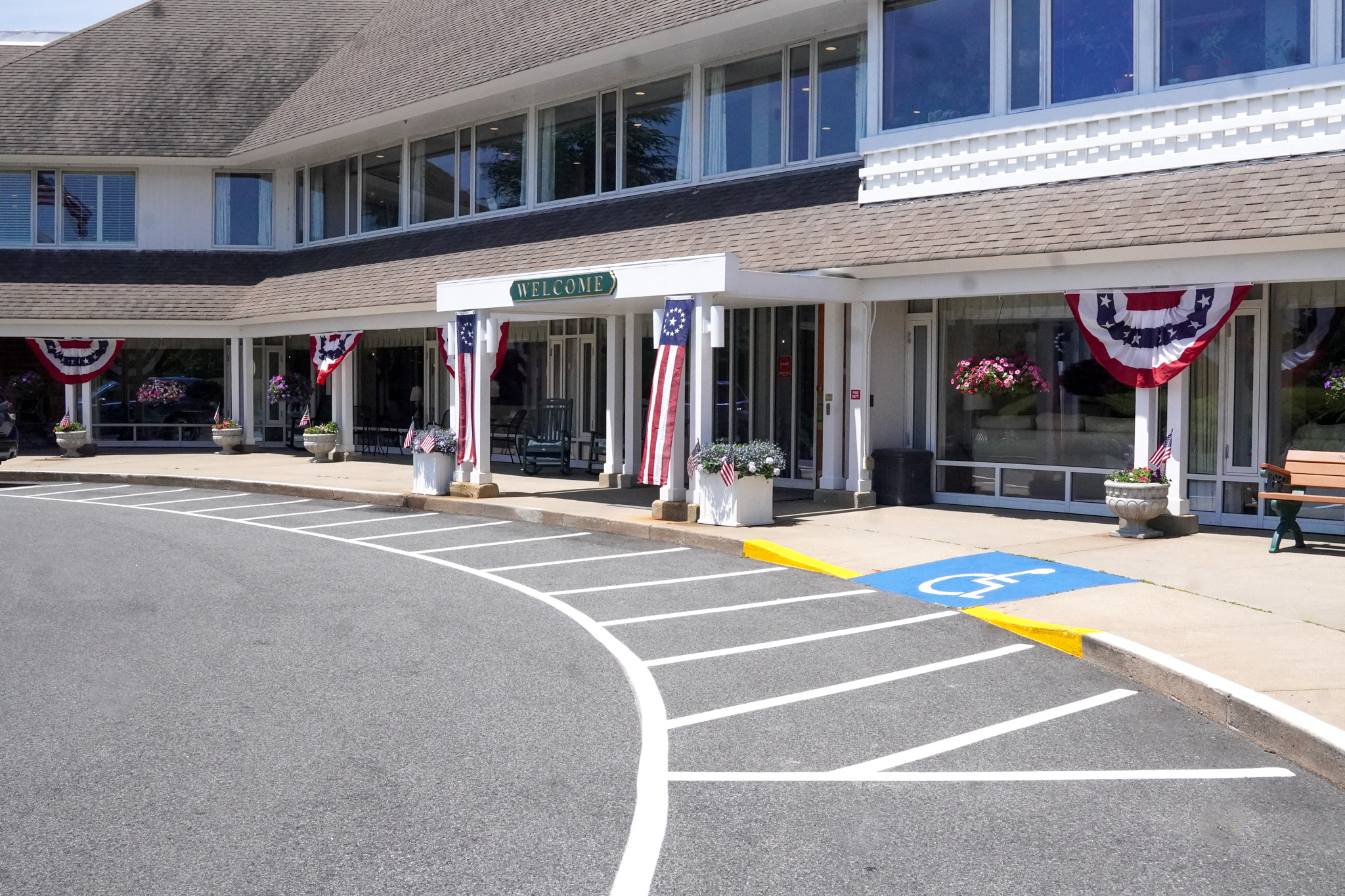 Building entrance with patriotic bunting, welcome sign, and accessible parking space in front, creating a festive summer atmosphere.
