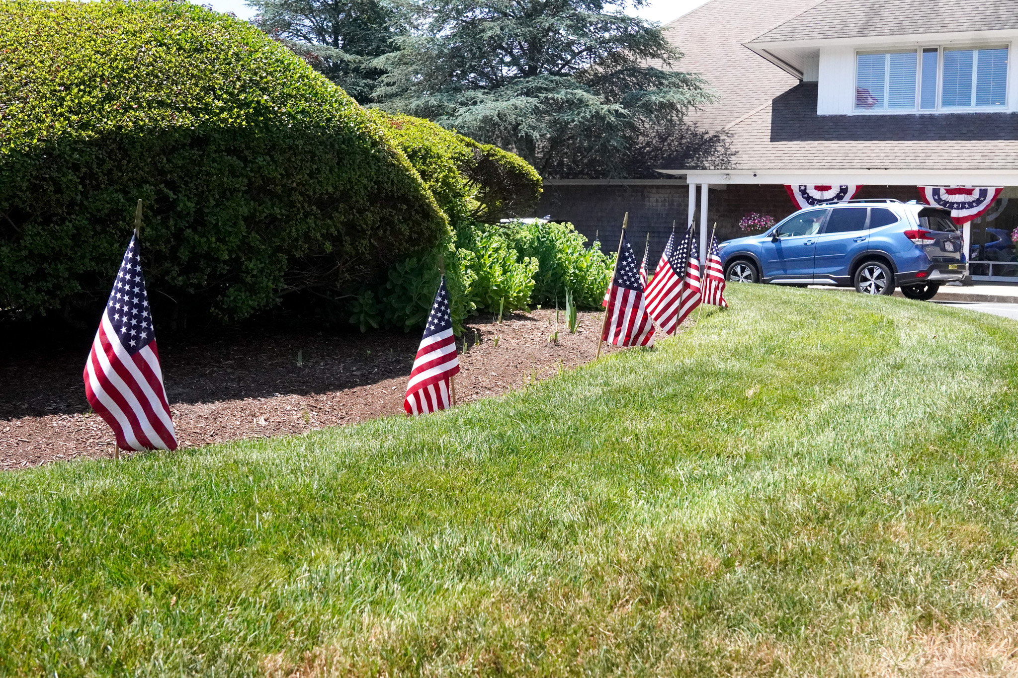 Small American flags line a garden in front of a house decorated for a patriotic summer celebration.