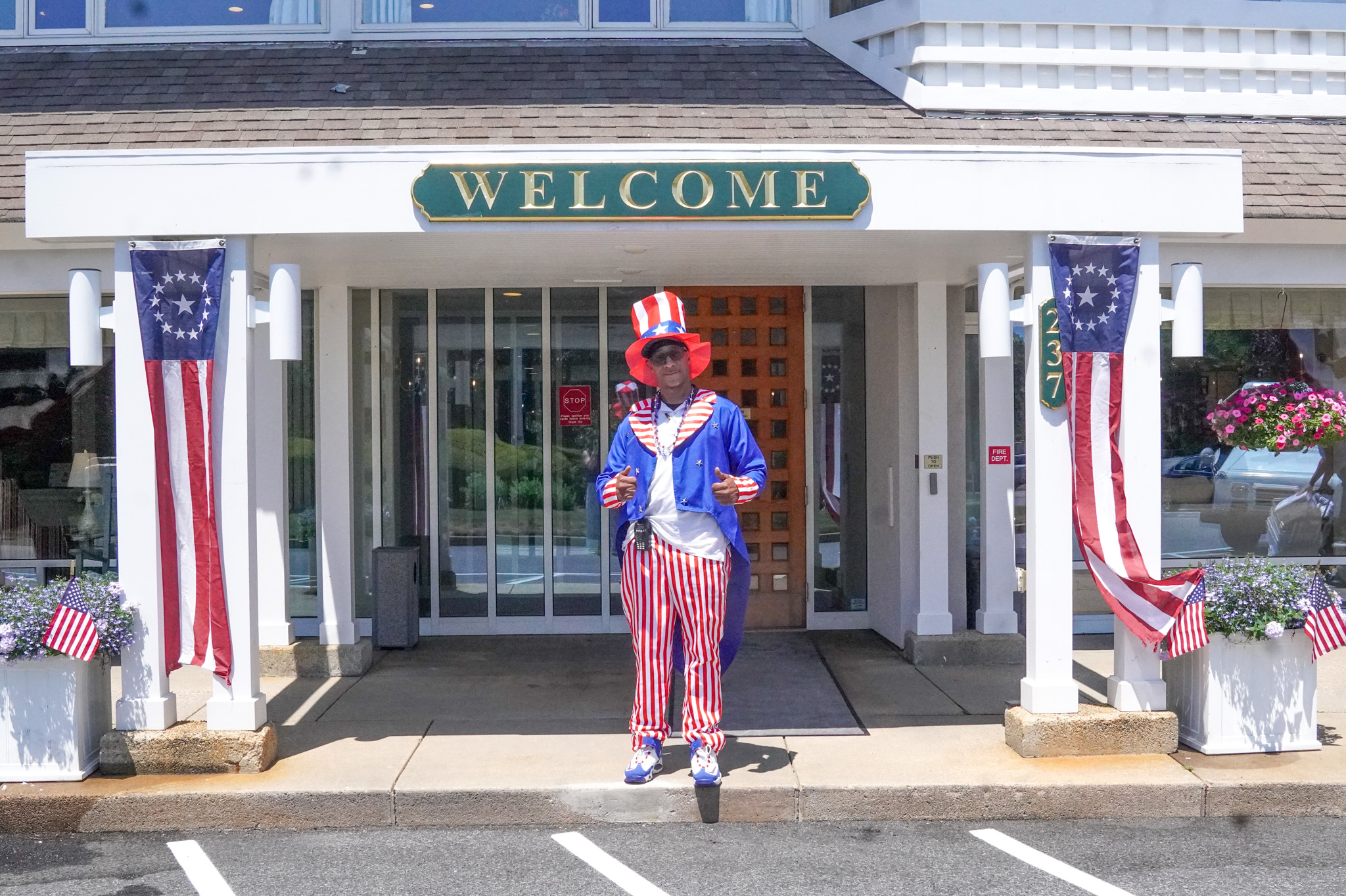 Person dressed as Uncle Sam stands in front of a building with a WELCOME sign and patriotic summer decorations.