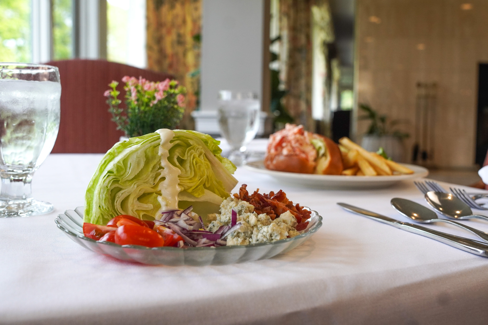 A wedge salad with crisp lettuce, tomatoes, bacon, red onion, blue cheese, and dressing on a table.