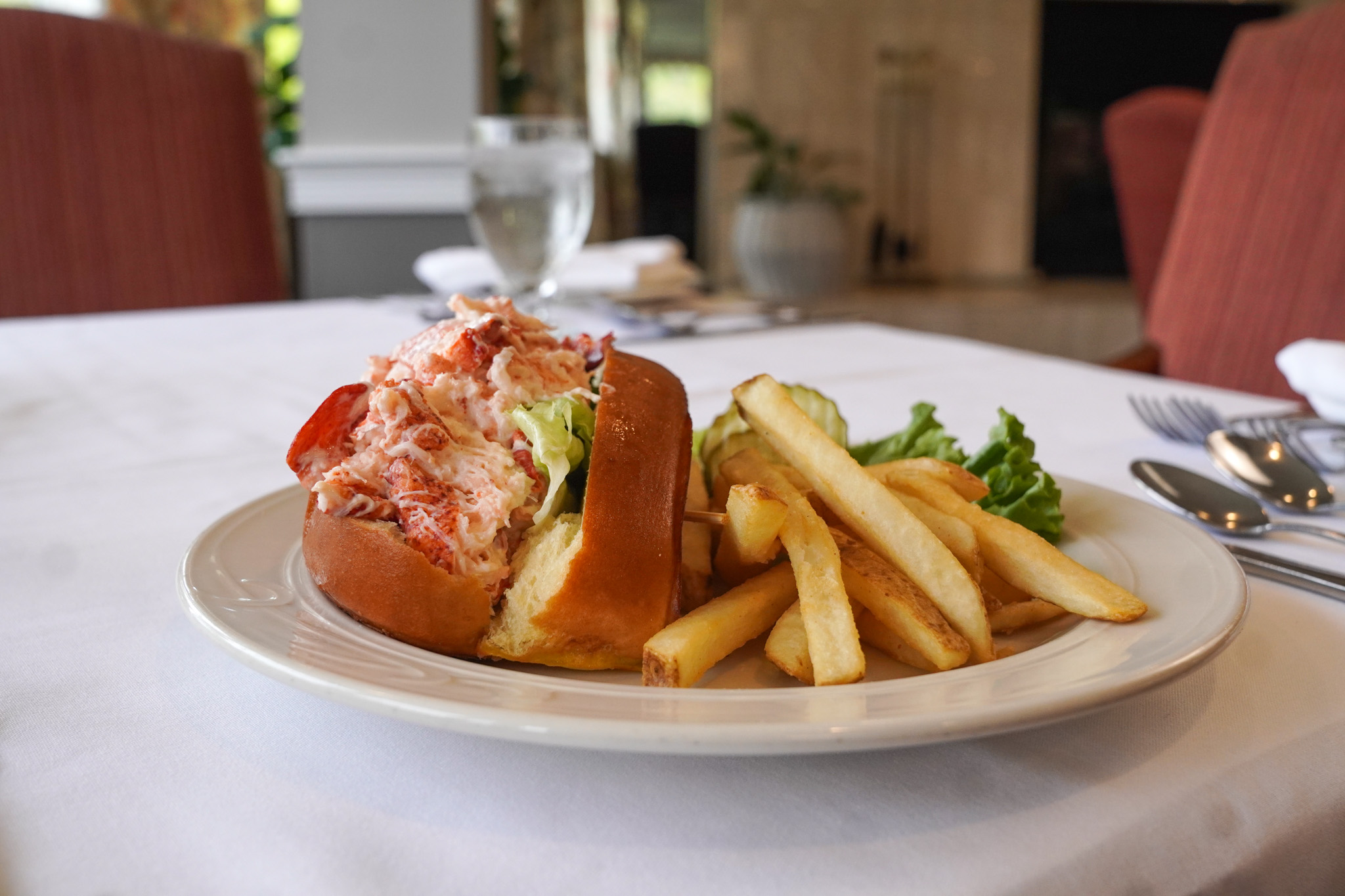 A lobster roll with lettuce and a side of French fries on a white plate, perfect for celebrating a birthday or enjoying comfort food when you're recovering from a cold and flu.