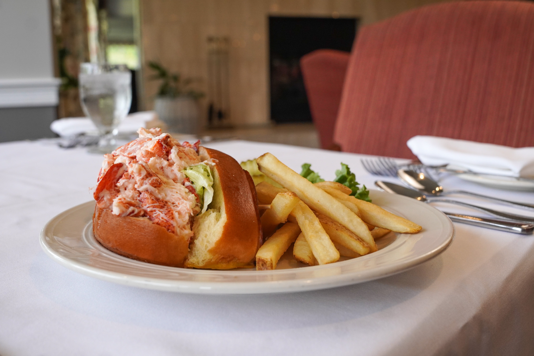 A lobster roll and French fries are artfully arranged on a white plate, showcasing the culinary appeal of this beloved animal from the sea, ready for dining.