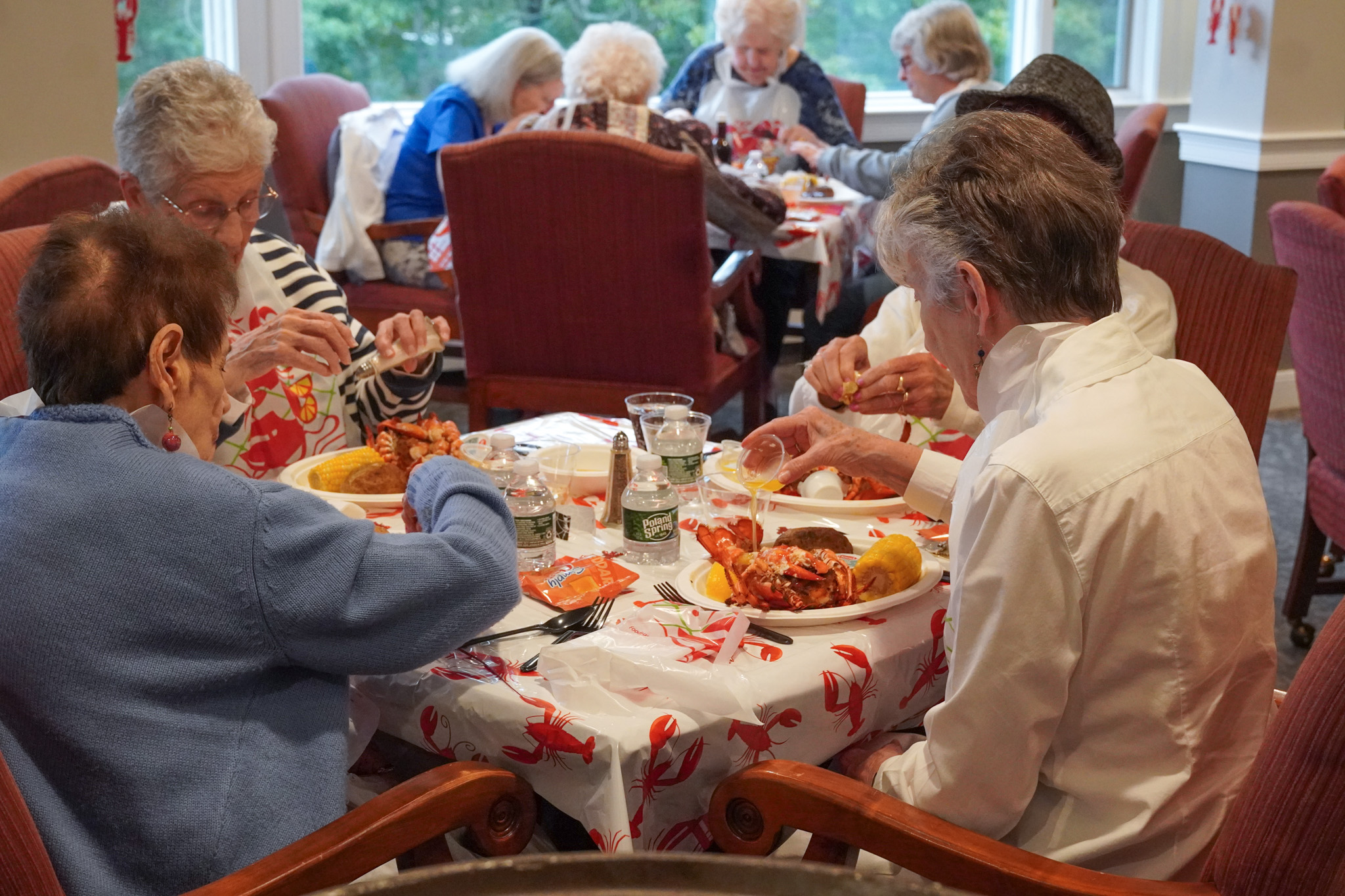 A group of elderly people, gathered around a table in a dining room, enjoy lobster together while reminiscing about past scholarship achievements.