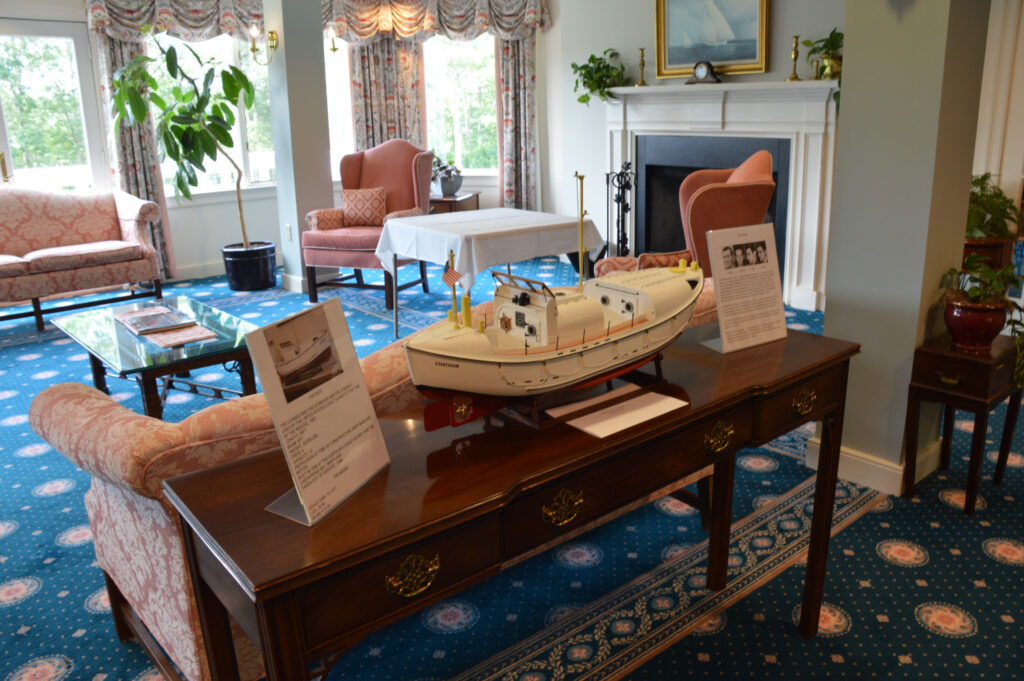 A model boat is displayed on a wooden table in a cozy, senior living space adorned with sofas and a welcoming fireplace.