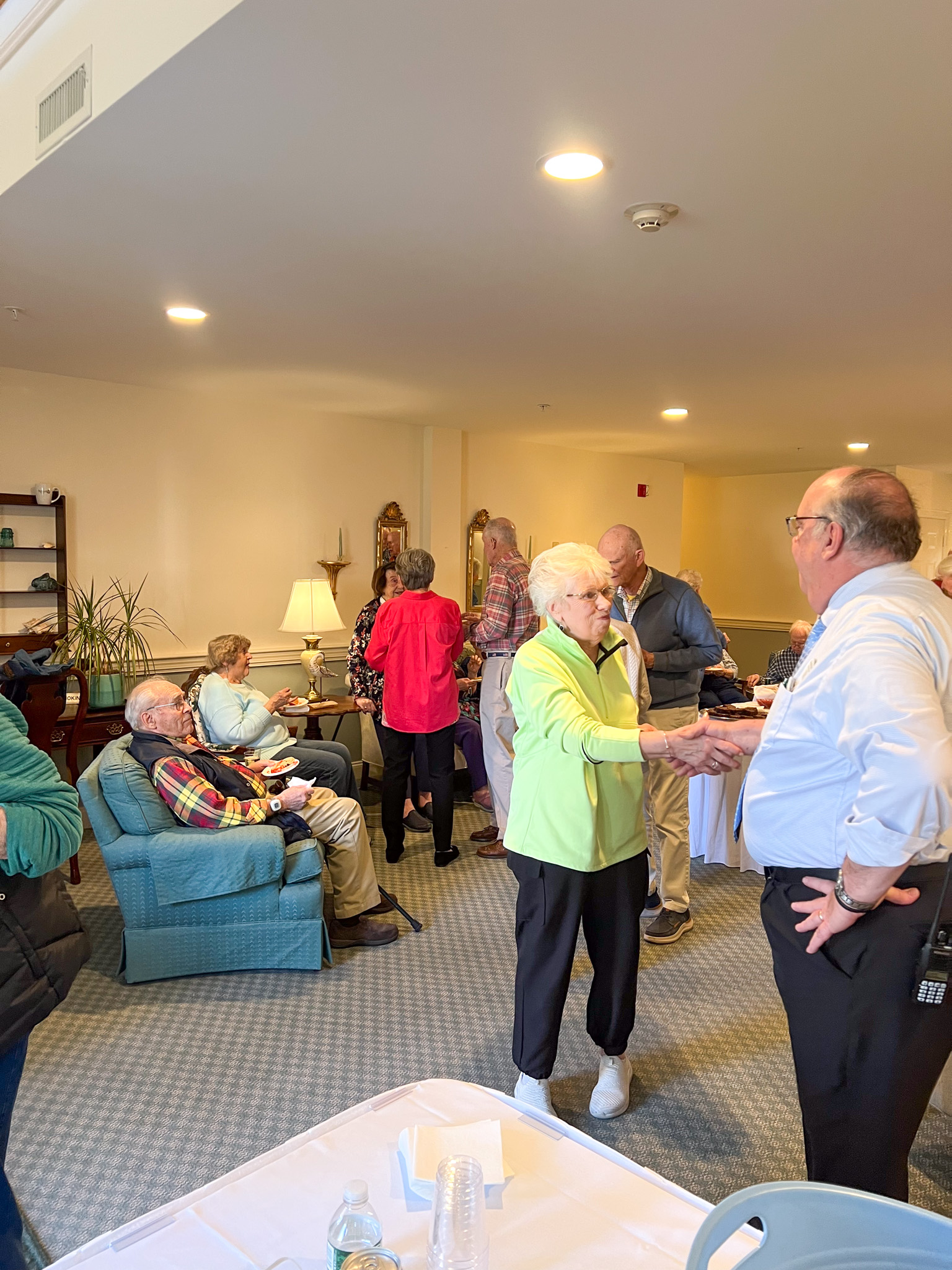 A group of seniors socialize in a well-lit room, celebrating a recent scholarship award, with two people shaking hands in the foreground.