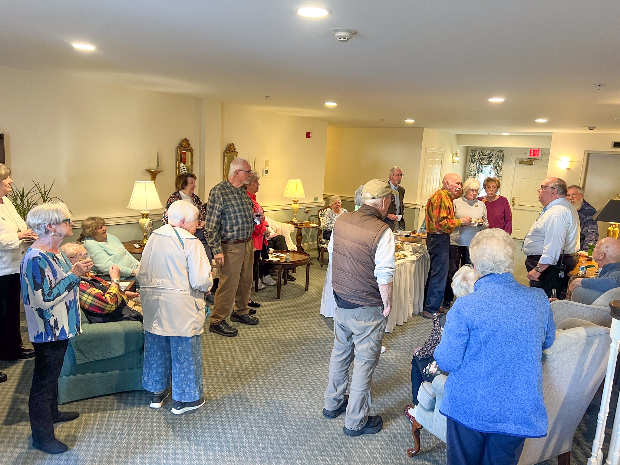 A group of elderly people gather and socialize in a cozy, well-lit living room, sharing stories and reminiscing about their past scholarship achievements.