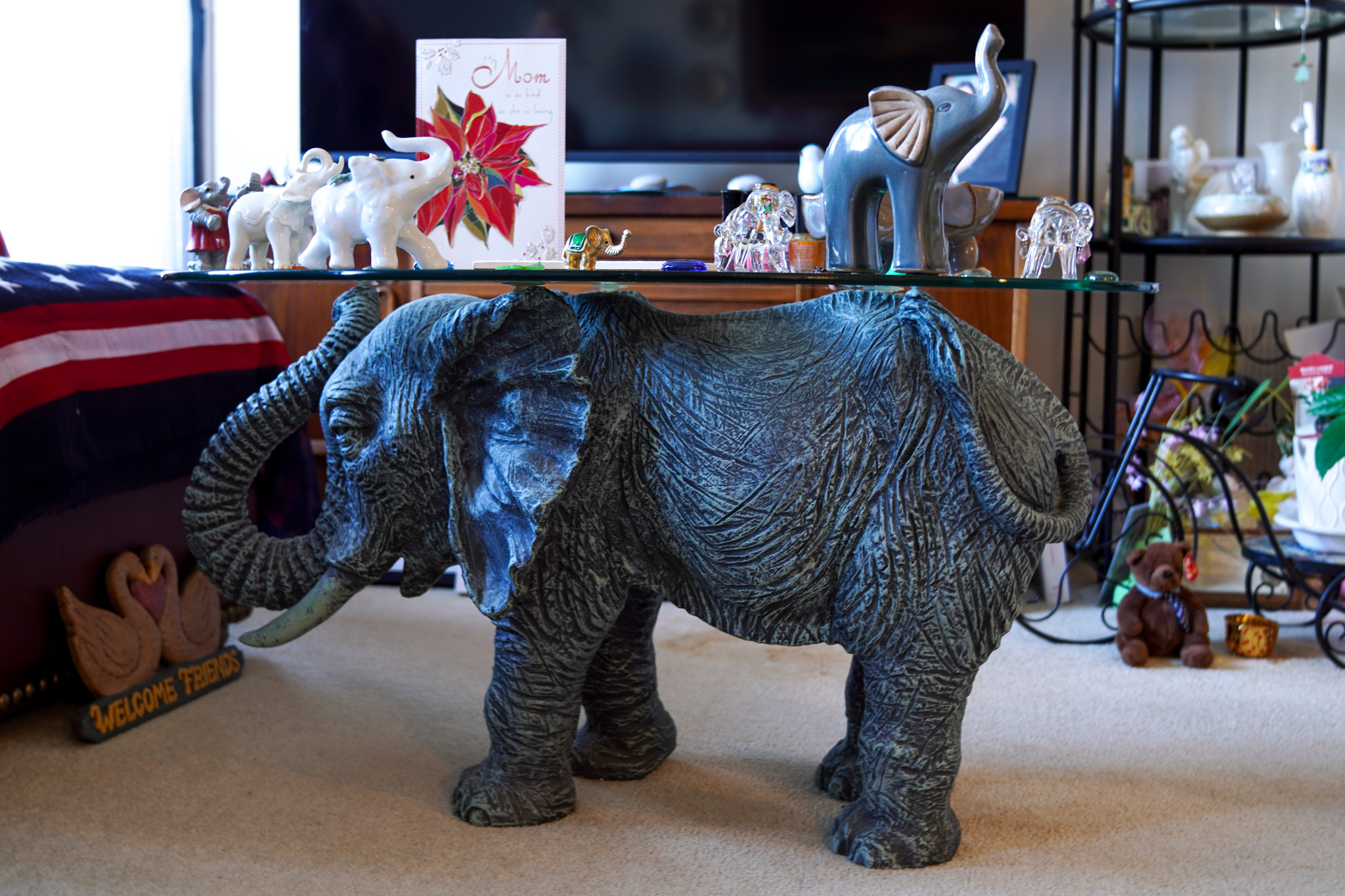 Elephant statue glass table with decorative elephants and a flower card displayed on top, alongside a charming bee motif, in a cozy living room.