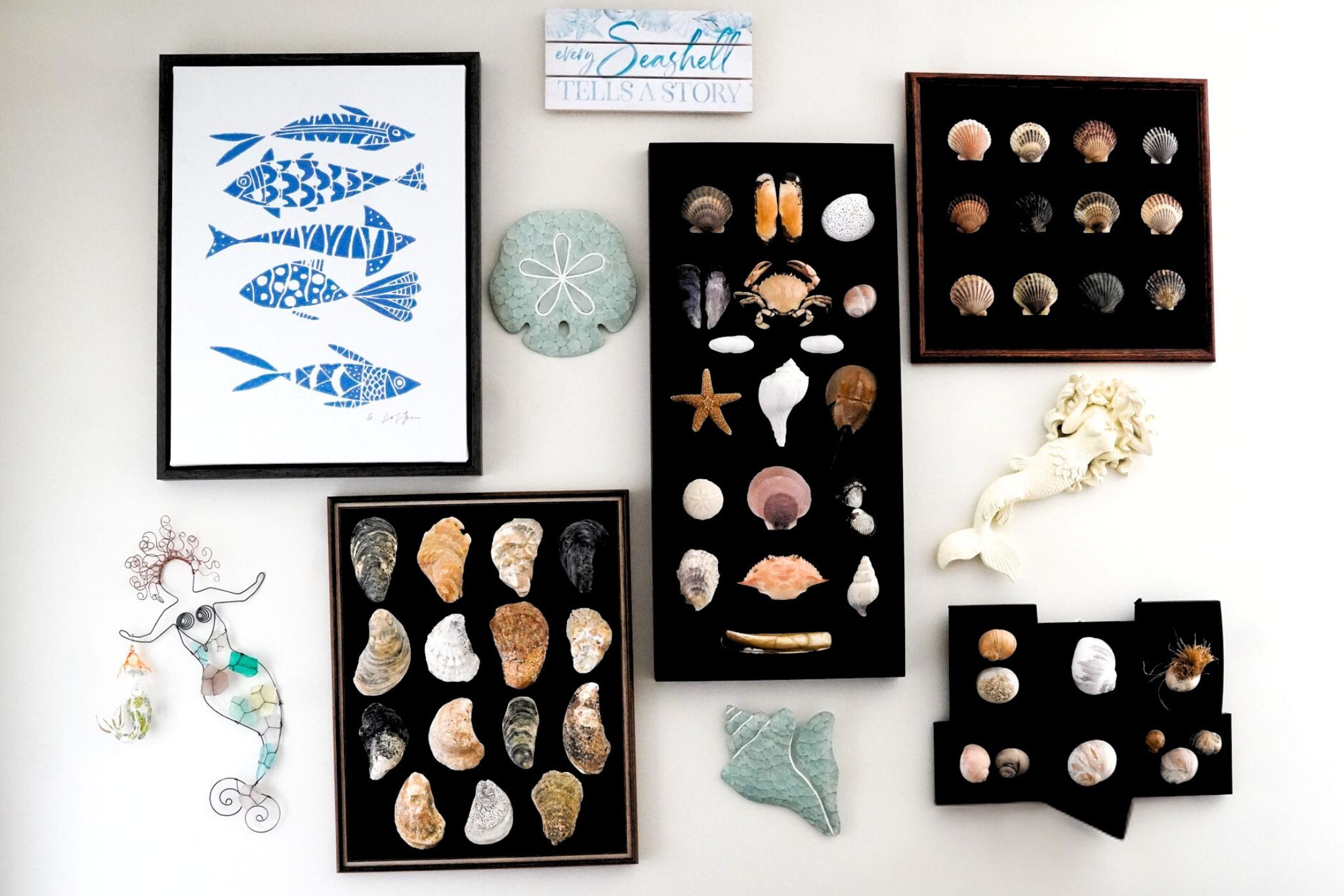 Wall art display with framed seashells, blue fish print, two mermaid decorations, and a sand dollar creates a charming Cape Cod-inspired look.