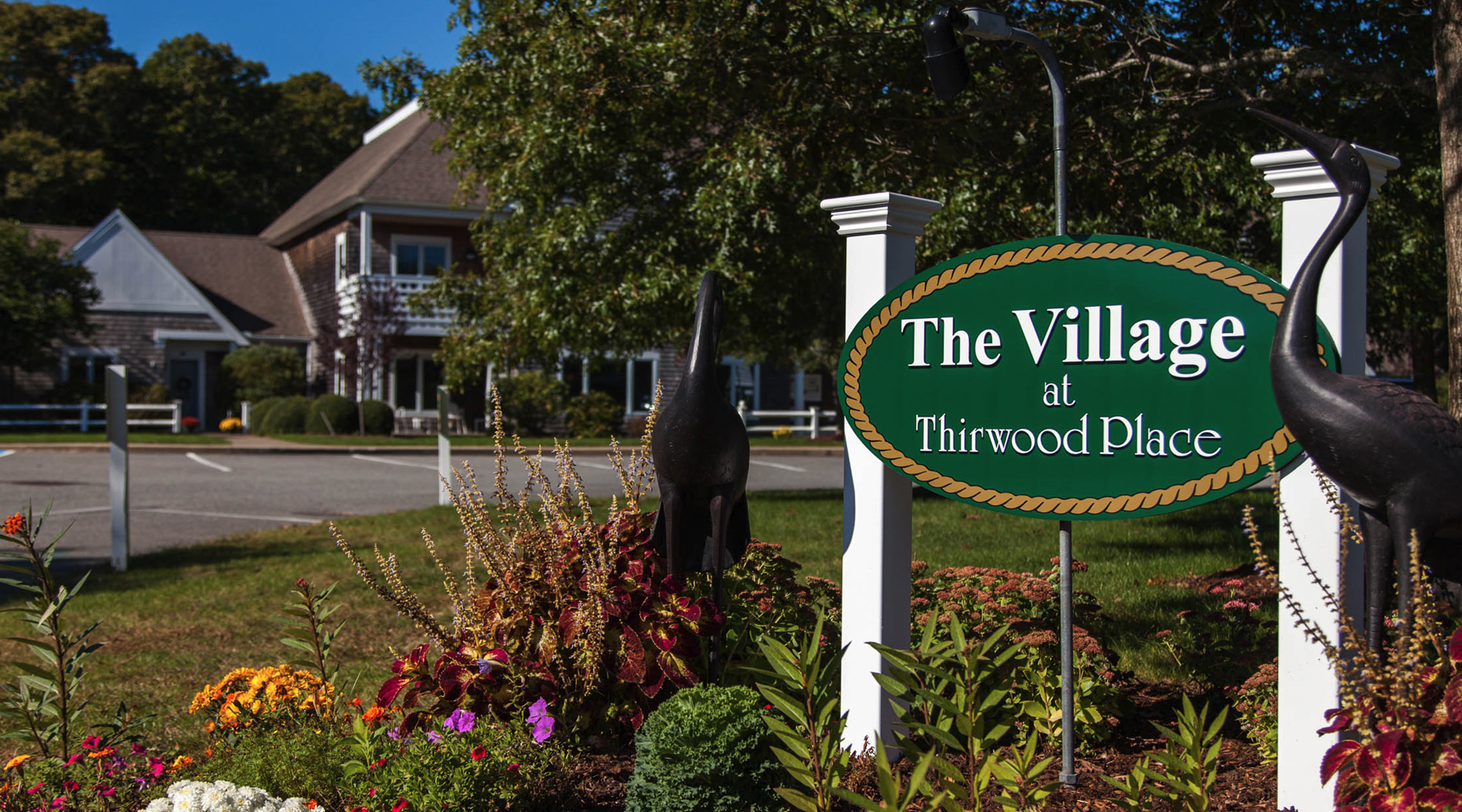 Sign reading The Village at Thirwood Place with flowers and a building in the background, capturing a classic Cape Cod charm.