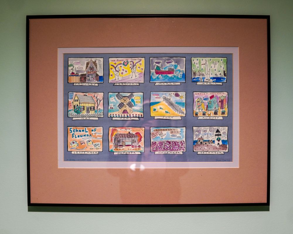 Framed artwork featuring twelve colorful, child-like drawings depicting various scenes adds a vibrant touch to the green wall, bringing joy and warmth to the senior living space.