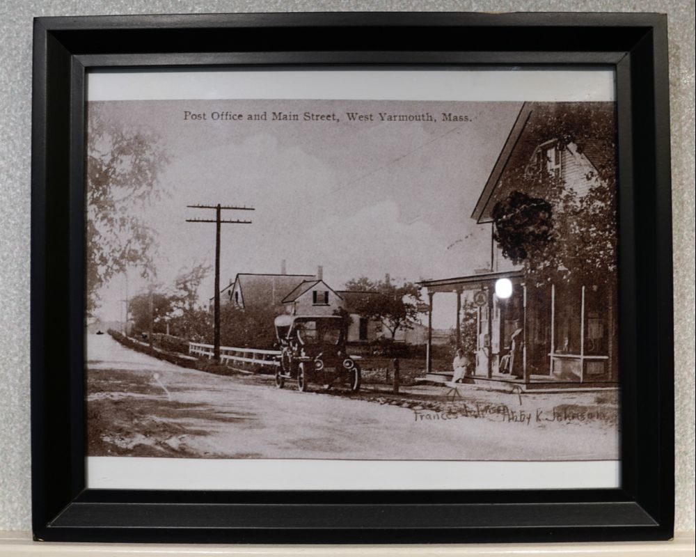 Framed vintage photo of Post Office and Main Street in West Yarmouth, Massachusetts, featuring an early automobile, evokes nostalgia and charm, reminiscent of simpler times—a treasured piece perfect for enhancing the ambiance of a senior living space.