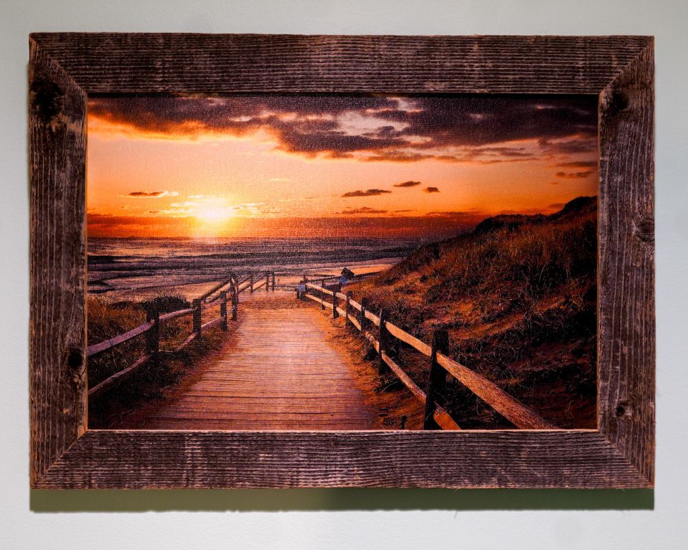 Framed painting of a boardwalk leading to the beach at sunset, with an orange sky and calm sea—a perfect piece for senior living spaces, capturing tranquility and serenity.